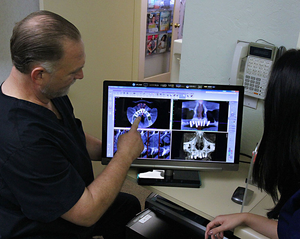 Dr. Cooper points to x-ray images of teeth on a computer screen while a woman observes