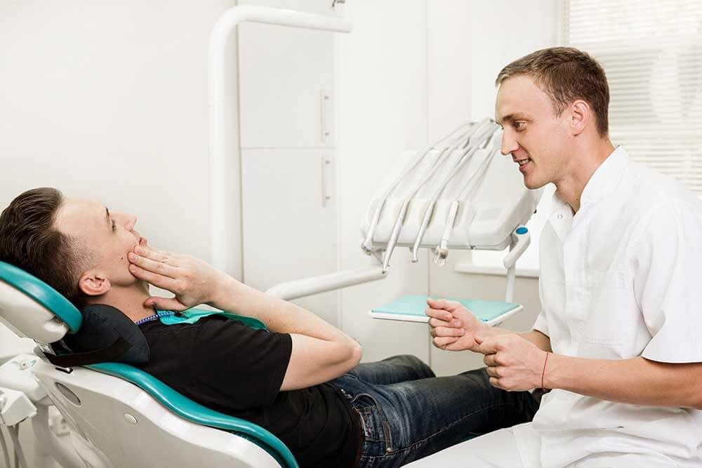 Doctor speaking with a patient who is sitting in the treatment chair holding the side of his face